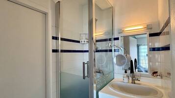 Un baño con cabina de ducha de vidrio, un lavabo blanco y un espejo.