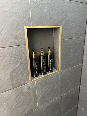 A bathroom with a shelf holding four toiletries: conditioner, body wash, and shampoo. - Peaceful Suite in charming Wilson,NC (Wilson)