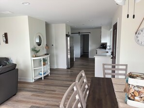 A modern kitchen with white cabinets, a wooden dining table, and a seating area with a dark sofa and a white console table.