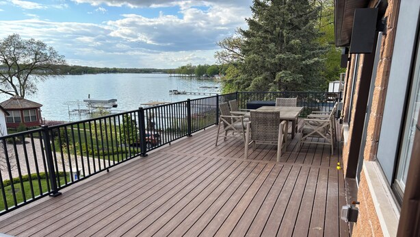 Eine Holzterrasse mit Tisch und Stühlen, mit Blick auf ein Gewässer und einen Steg.
