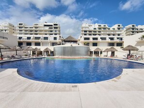 A swimming pool with lounge chairs and umbrellas, surrounded by multi-story buildings. -  Cancún Caribe Soul studio /walk on beach/ Top Location (Cancún)