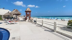 Un resort en la playa con piscina, sillas de descanso y una estructura de techo de paja.