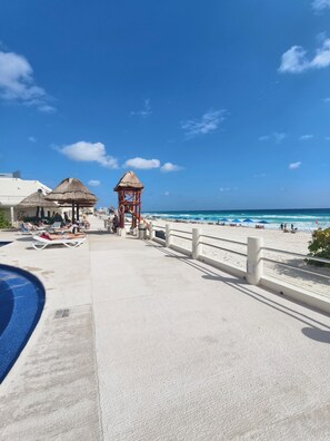Un complexe hôtelier situé en bord de mer, doté d’une piscine, de chaises longues et d’une tour de surveillance pour les sauveteurs.