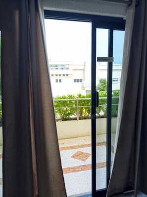 Uitzicht door een raam met gordijnen, een balkon en een gebouw op de achtergrond.
