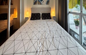 Ein Bett mit geometrischem Muster auf der Bettdecke, Nachttischlampen, ein Nachttisch und ein Fenster mit Blick.