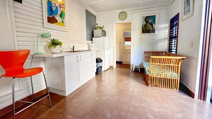 Eine moderne Küche mit weißen Schränken, einem roten Stuhl, einem Holz-Babybett und einem Gemälde an der Wand.
