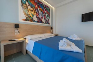 A hotel room with a bed, a bedside table with a remote control, a wall-mounted TV, and a large colorful painting above the bed. - Alexandr Tiffany House (Pizzo)