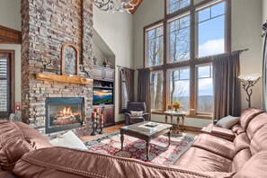 A spacious living room with a fireplace, leather sofa, and large windows offering a view. - Ridge Haven Lodge at Echota (Banner Elk)