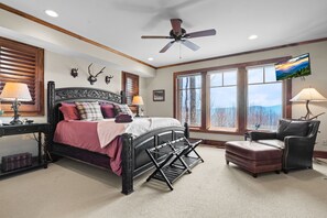 A bedroom with a bed, a chair, a desk, a ceiling fan, and large windows. - Ridge Haven Lodge at Echota (Banner Elk)
