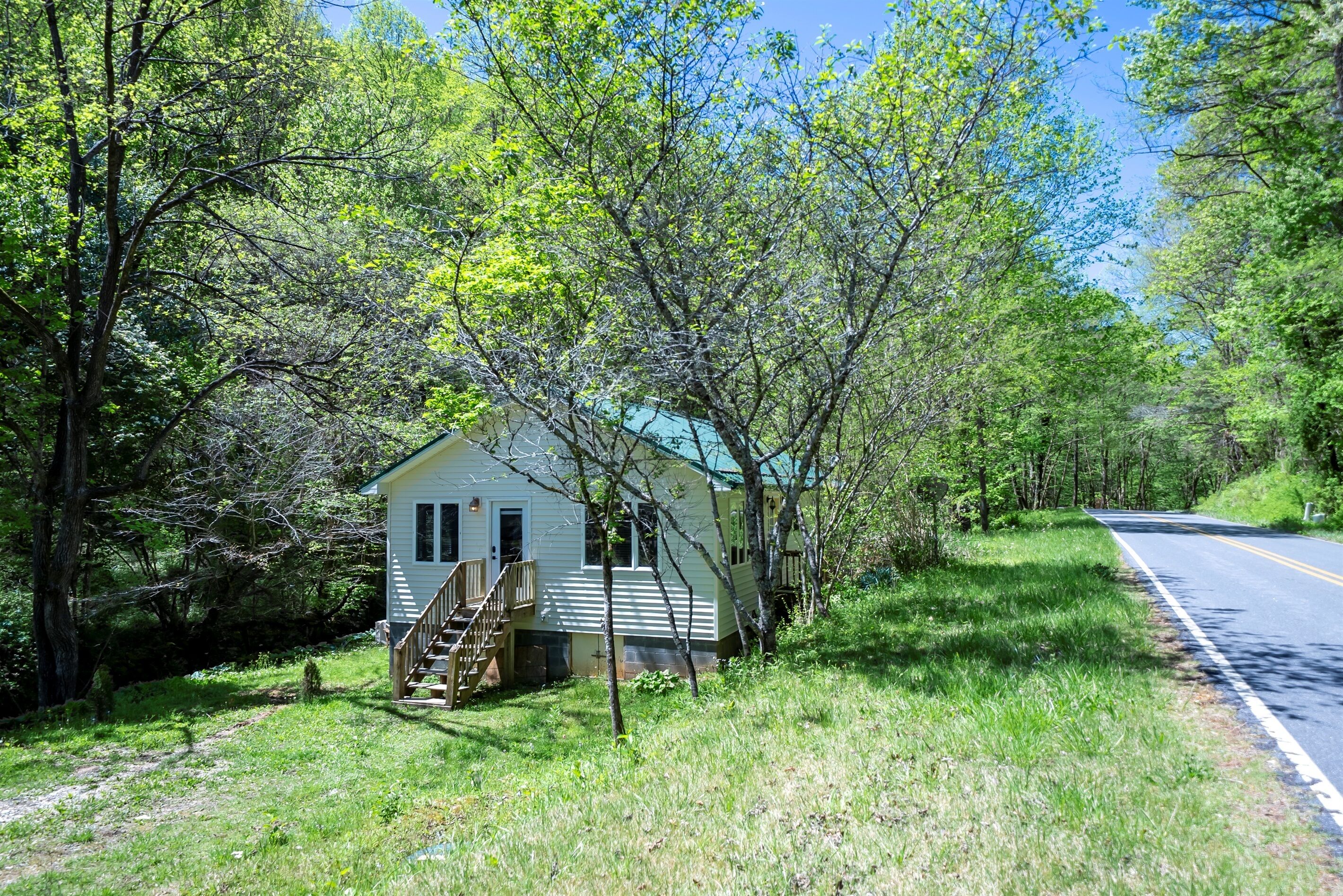 A small house with a porch and stairs, surrounded by trees and a road.