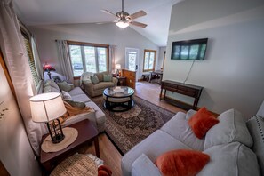 A living room with a ceiling fan, a television, a sofa, a coffee table, and a dining area. - Creekside Living | Fish, Relax, Recharge (Robbinsville)