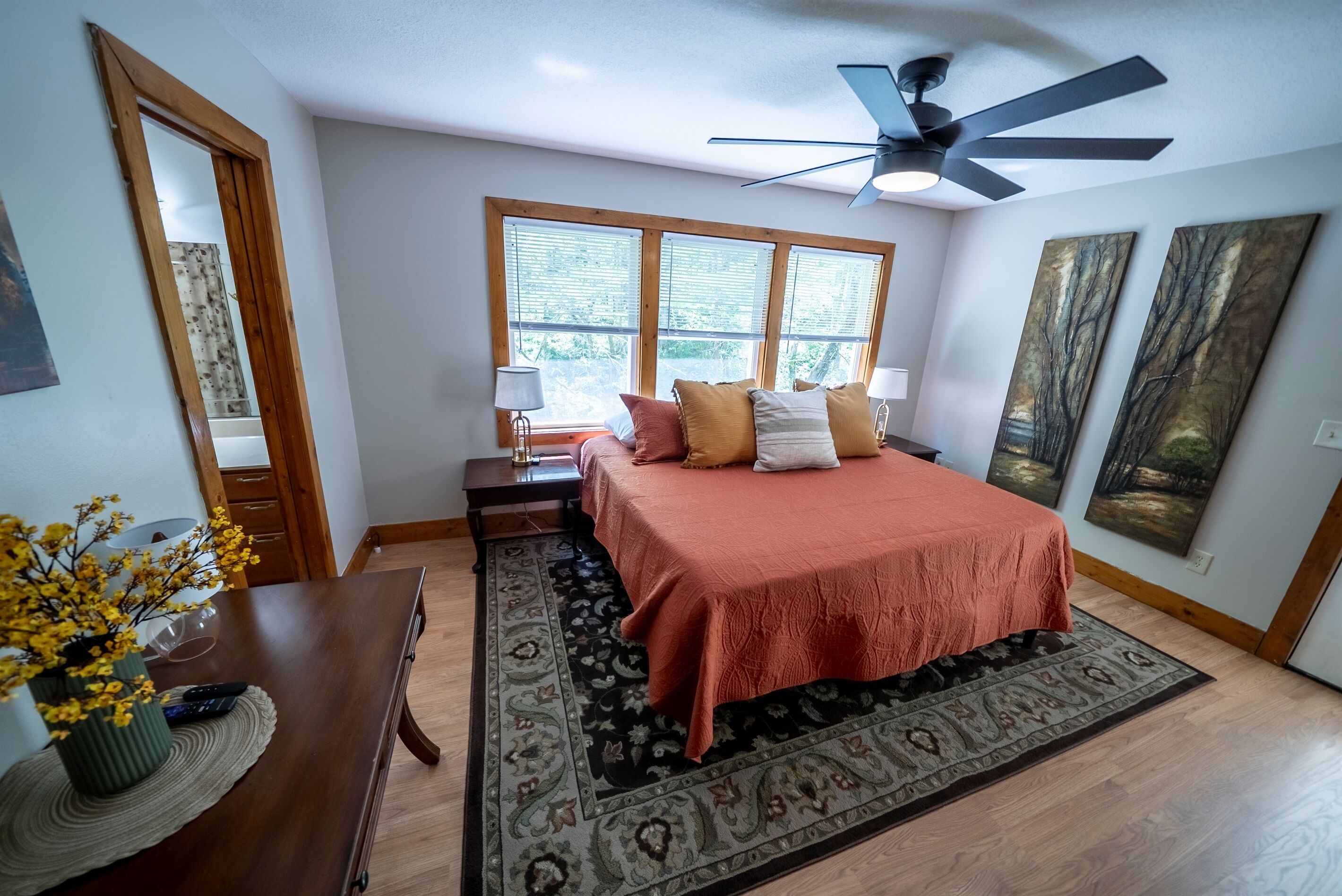 A bedroom with a bed, a ceiling fan, a window, a nightstand, and a painting on the wall.