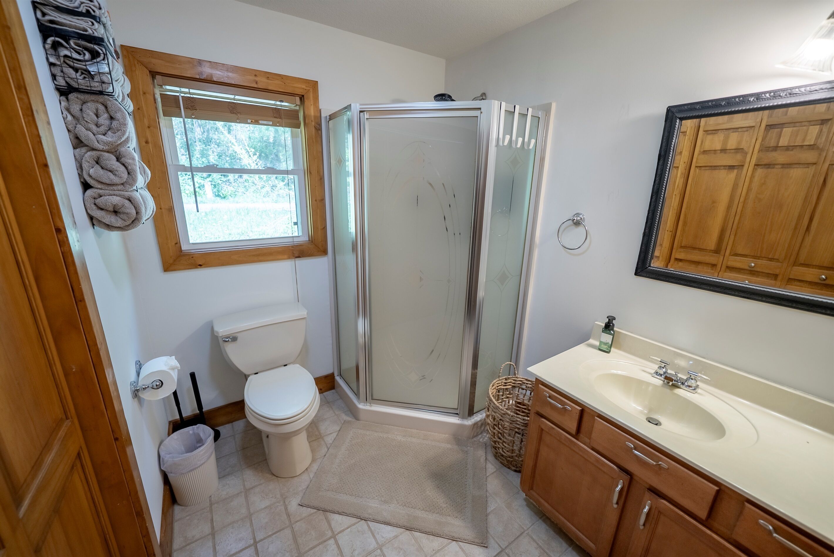 A bathroom with a toilet, shower, sink, and a window.