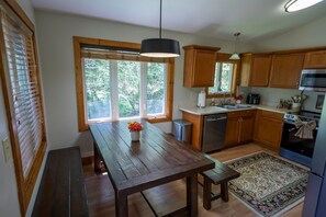 A kitchen with wooden cabinets, a stainless steel sink, a built-in oven, and a dining area with a bench and table. - Creekside Living | Fish, Relax, Recharge (Robbinsville)