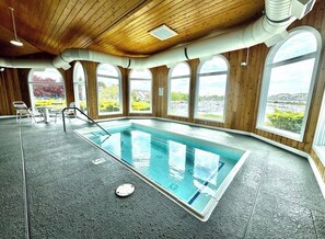 An indoor swimming pool with a view of the city, wooden walls, and a ceiling with ventilation ducts.