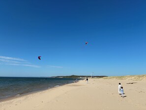 Una playa con cielos despejados, aguas tranquilas y algunas personas caminando por la orilla.