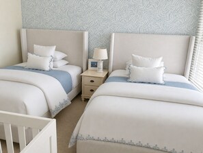 Habitación de hotel con dos camas, una mesita de noche con lámpara y una cuna.