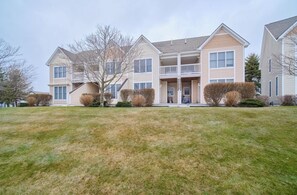 A two-story residential building with a front porch, multiple windows, and a well-maintained lawn.