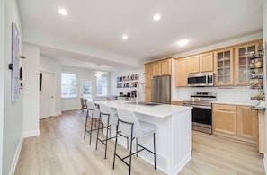 A modern kitchen with a central island, bar stools, wooden cabinets, and built-in appliances.