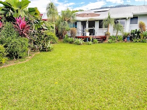 A well-maintained lawn, a house with a porch, and various tropical plants. - The Buddha Studio, modern & private, moments from Cairns cultural hub & airport. (Whitfield)