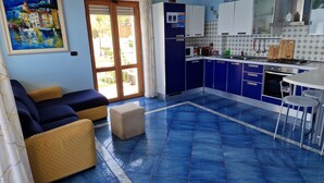 A living room with a sofa and ottoman, a kitchen with blue cabinets, and a painting on the wall.