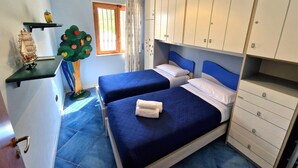 A bedroom with two beds, a wardrobe, a small window, and a decorative tree.
