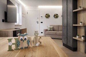 A modern living room with a wooden table, a sofa, and a TV mounted on the wall. - Mountain Home Fiemme (Castello-Molina di Fiemme)