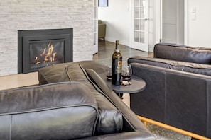 A modern living room with a fireplace, leather sofas, a small table with a bottle and glasses, and a door leading to another room. - Yakima Valley Views with Pool and Sauna (Yakima)