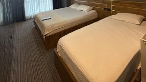 Hotellihuone, jossa on kaksi sänkyä, suuri ikkuna, jossa on verhot, kattovalaisin ja seinälle asennettu termostaatti.