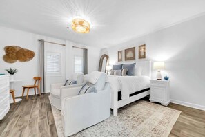 Ein Schlafzimmer mit Bett, Nachttischen, einem Sessel, einem Schminktisch und einer Deckenleuchte.