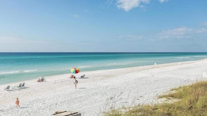 Ein Strand mit weißem Sand, einigen Liegestühlen und einem bunten Sonnenschirm.