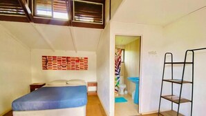 Un dormitorio con cama, repisa montada en la pared y baño visible a través de una puerta abierta.