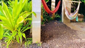 Un espacio al aire libre techado con un pilar de hormigón, una hamaca y abundante vegetación verde.