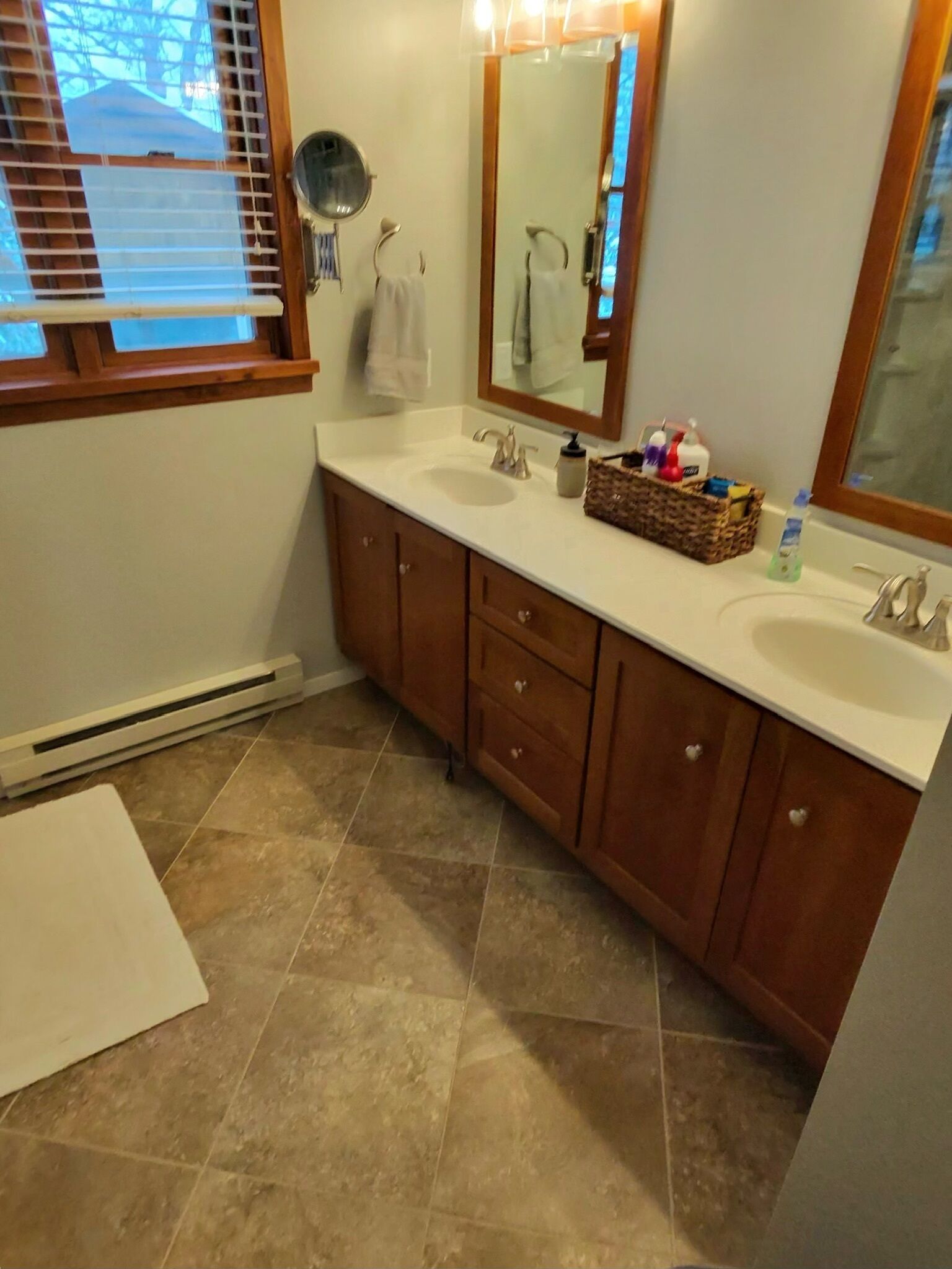A bathroom with two sinks, a mirror, and a window with blinds.