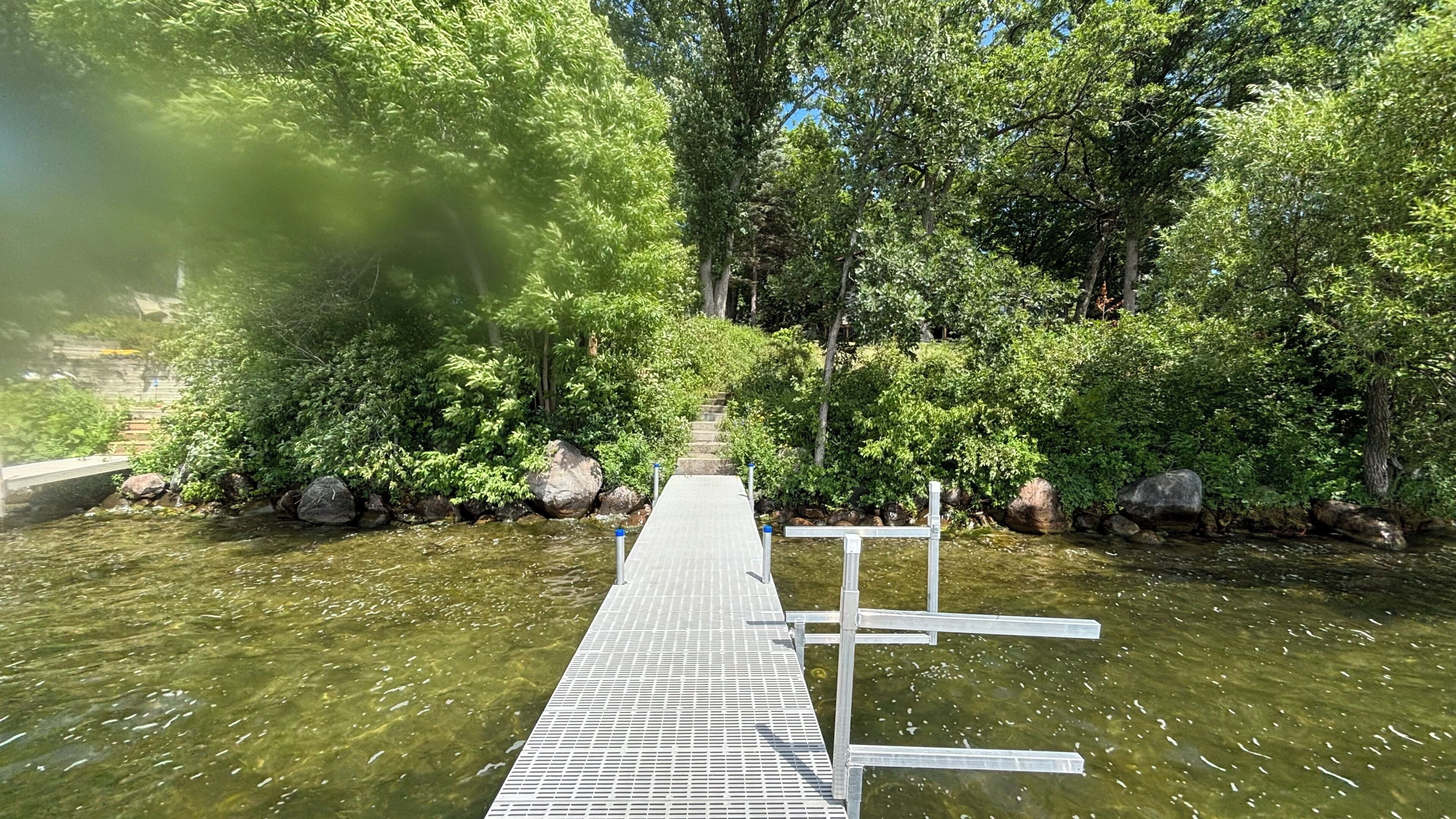 A wooden dock extending into a calm body of water, surrounded by dense greenery and trees.