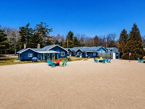 A row of blue cabins with outdoor seating areas and a sandy beach in the foreground.