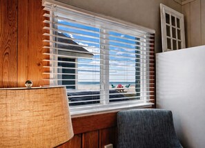 A room with a window overlooking a beach, a wooden cabinet, and a chair.
