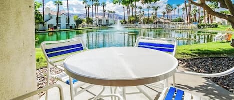 A poolside area with a round table and chairs, a fountain, and a view of palm trees and buildings.