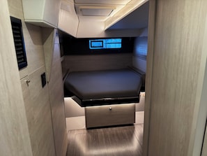A compact room with a bed, a control panel, and a small storage drawer.