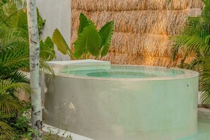 A circular pool with a concrete edge, surrounded by lush greenery and a thatched wall in the background. - Villa · Pools Privadas · Rooftop · Selva Tulum (77760)