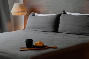 A bed with grey bedding, a wooden headboard, a woven lamp, and a croissant on a wooden tray. - Villa · Pools Privadas · Rooftop · Selva Tulum (77760)