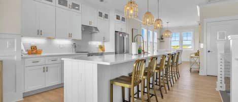 A modern kitchen with white cabinetry, a central island with bar stools, pendant lighting, and a large window.