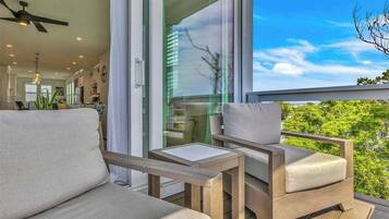 Un balcón con sofá y sillones, un ventilador de techo y vistas al verdor.