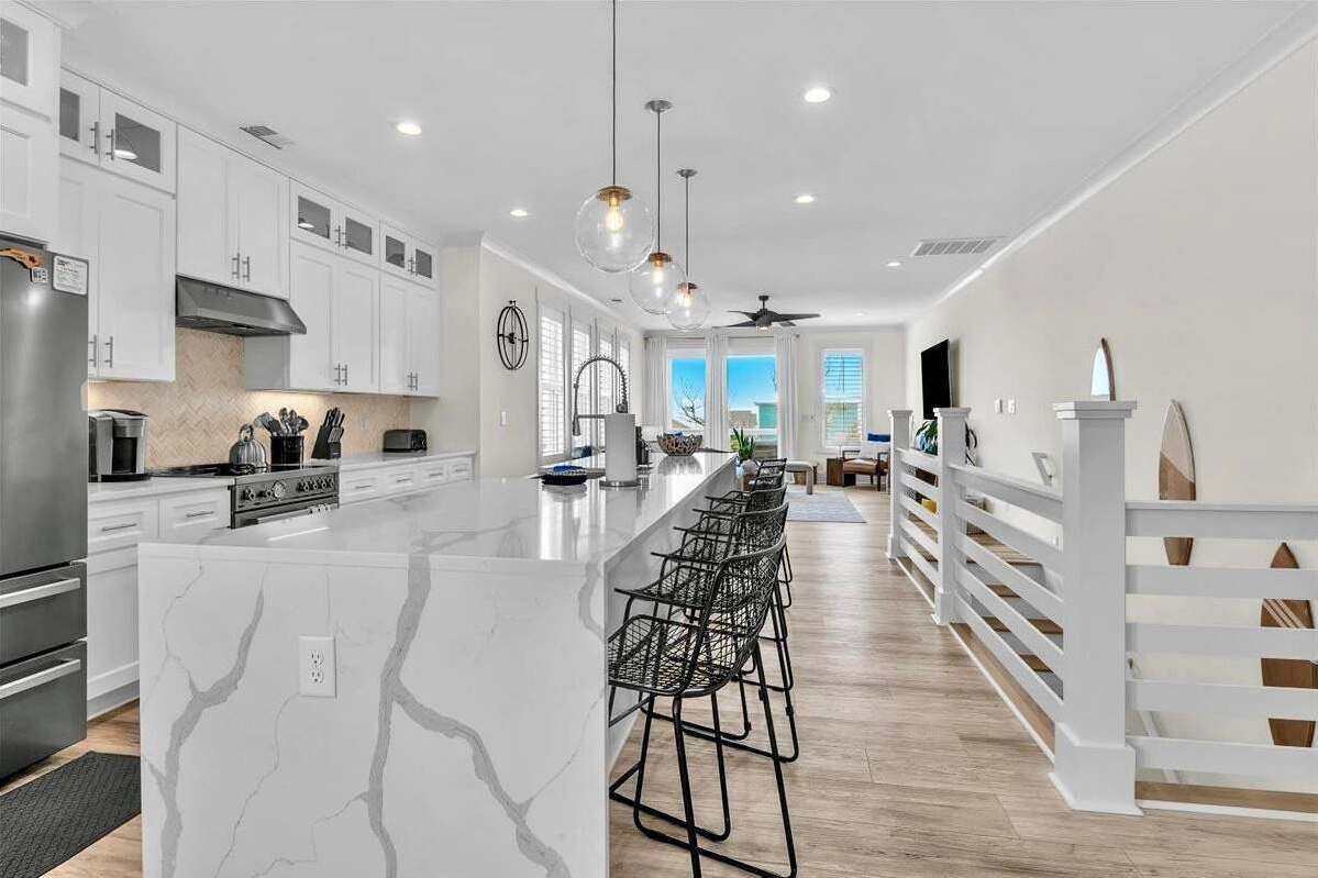 Una cocina moderna con gabinetes blancos, una isla de mármol y una amplia zona con taburetes.