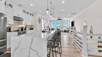 Una cocina moderna con gabinetes blancos, una isla de mármol y una amplia zona con taburetes.