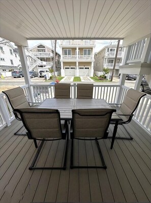 A covered outdoor patio with a table and chairs, overlooking a residential area with multi-story buildings and parked cars. - Steps to the Sand: Bright, Spacious Condo on South-End Beach Block (Ocean City)