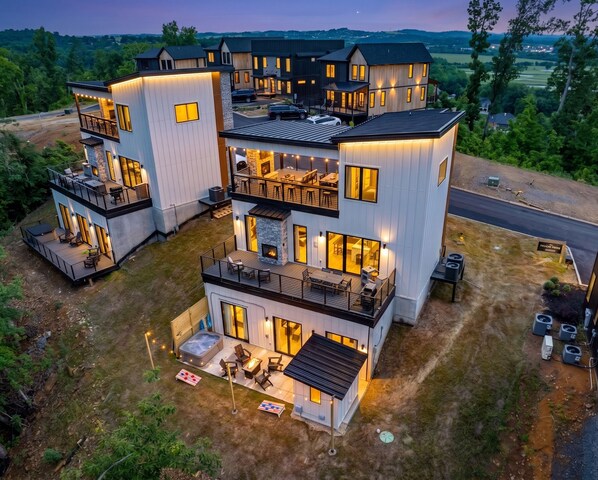A multi-story modern house with outdoor seating, a fireplace, and a view of the surrounding landscape. - Brand-New Retreat | Rooftop Deck, Sauna, Hot Tub, Game Room, Mountain Views (Sevierville)