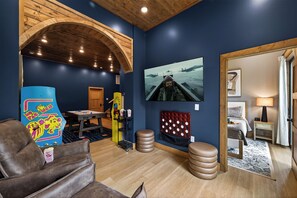A room with a wooden ceiling, a large screen, a couch, a small table, and a bed. - Brand-New Retreat | Rooftop Deck, Sauna, Hot Tub, Game Room, Mountain Views (Sevierville)