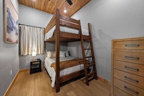 A bunk bed with a ladder, a bedside table with a lamp, a wooden dresser, and a painting on the wall. - Brand-New Retreat | Rooftop Deck, Sauna, Hot Tub, Game Room, Mountain Views (Sevierville)