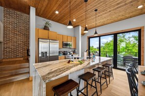 Cozinha moderna com ilha grande, eletrodomésticos de aço inoxidável e vista para um deck externo.